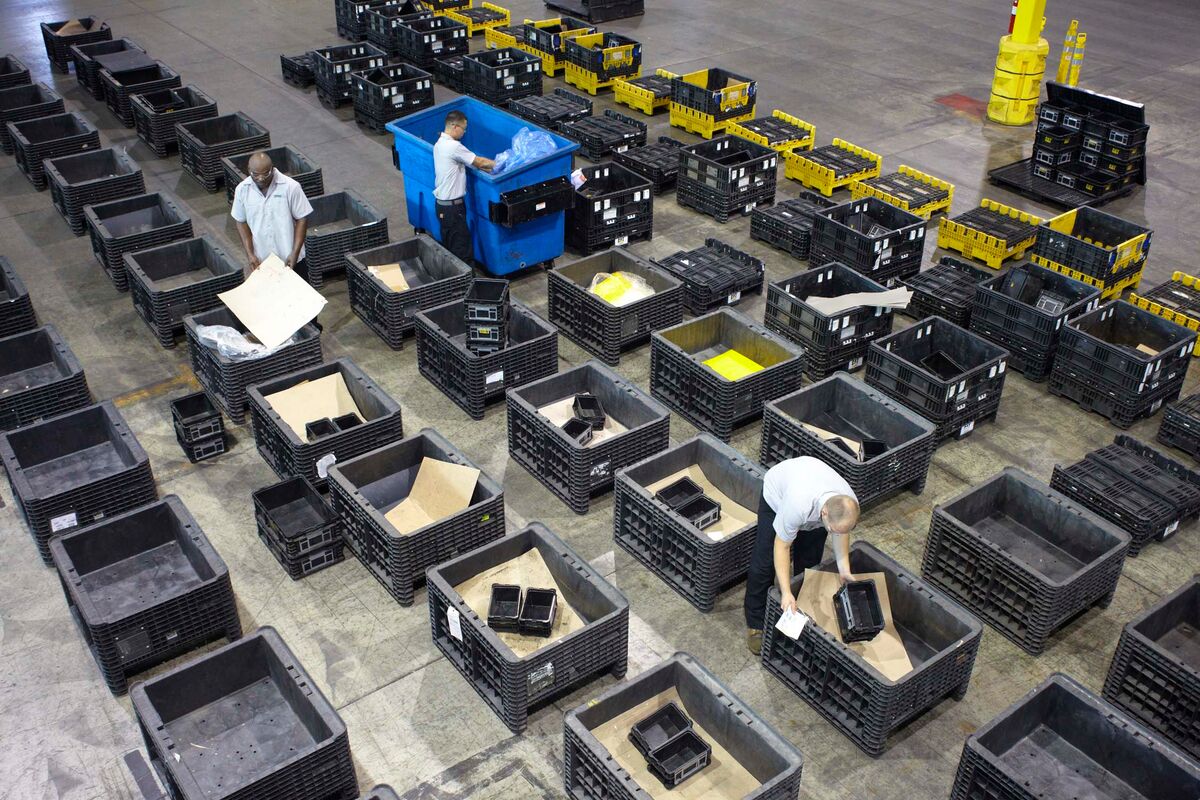 Workers sorting and organizing black bins in a large warehouse, surrounded by stacks of empty and filled containers.