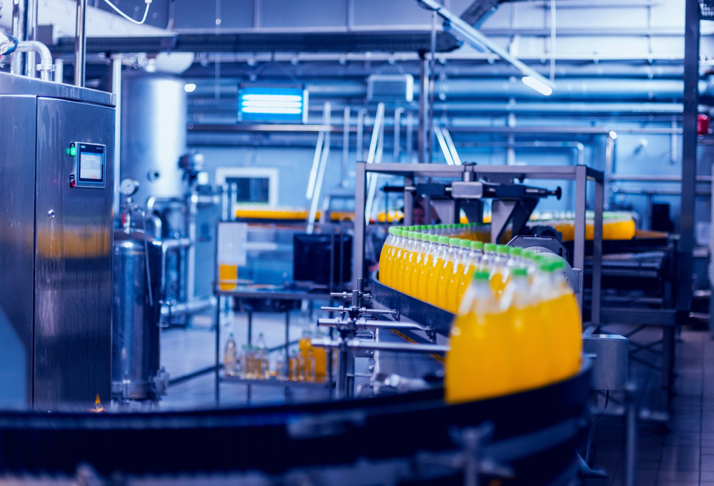 Assembly line in a beverage factory with rows of bottles being filled and capped, surrounded by industrial equipment and machinery.