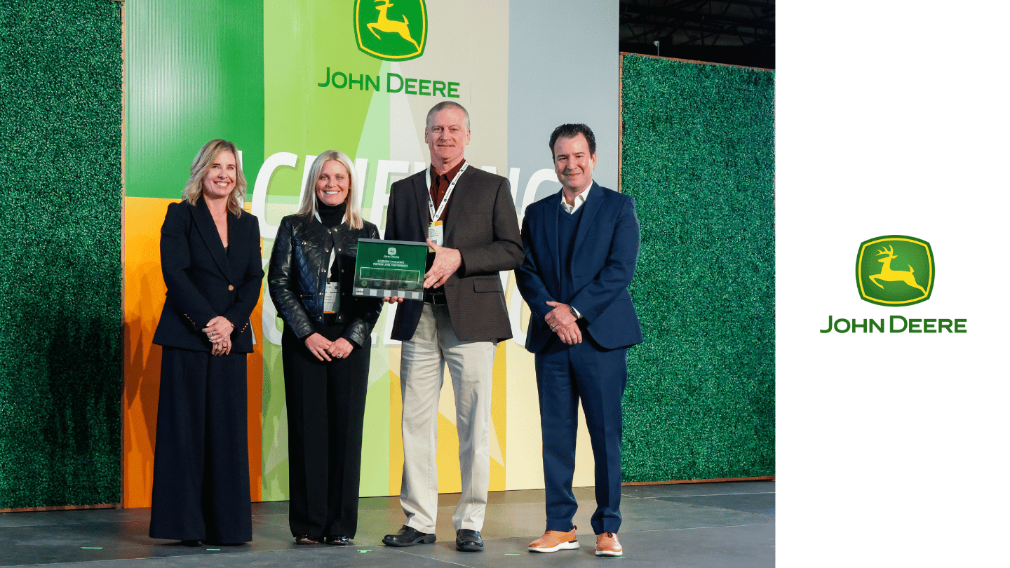 Four people stand on stage in front of a John Deere backdrop, with one person holding a plaque, highlighting ORBIS as a Partner-level Supplier and recipient of the John Deere Sustainability Award.