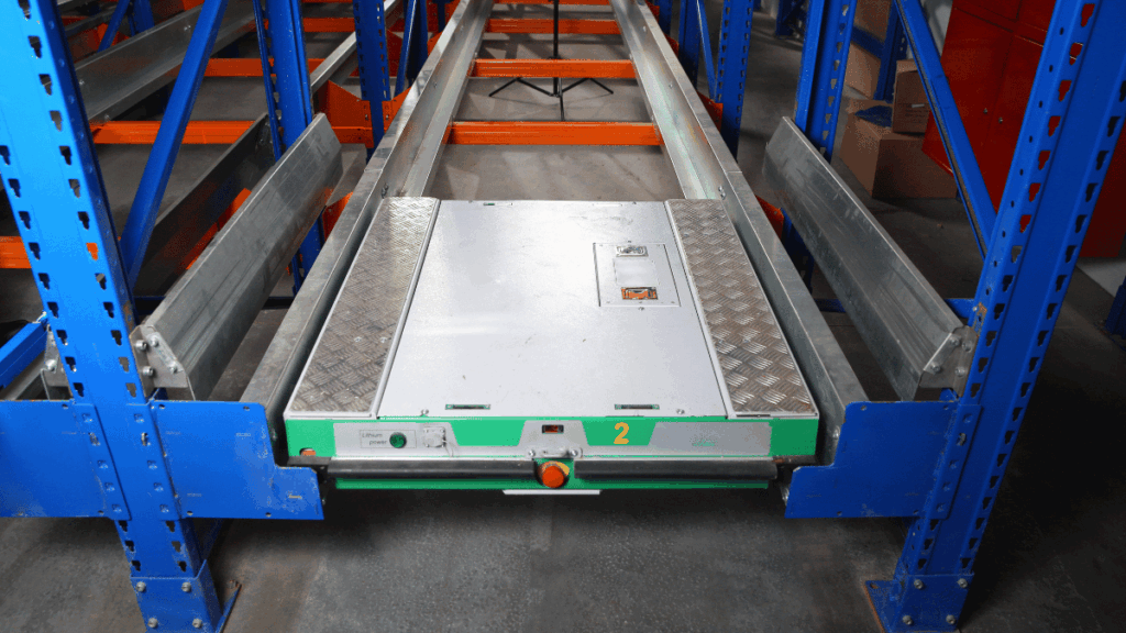 A close-up view of an automated shuttle system on rails between blue warehouse pallet racks, showcasing advanced material handling in storage facilities.